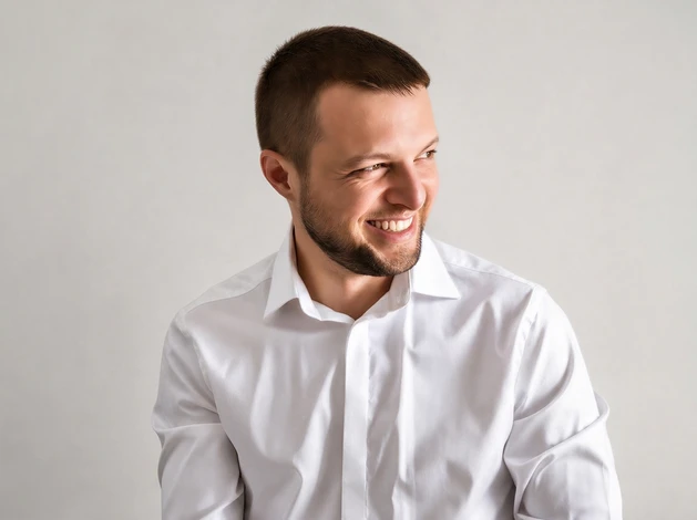 Portrait professionnel rapproché d'un homme d'âge mûr aux cheveux grisonnants, portant une chemise blanche professionnelle, debout dans une salle de formation lumineuse avec supports pédagogiques flous en arrière-plan, regard direct vers l'objectif, sourire serein et confiant, exprimant l'expertise et la bienveillance d'un formateur expérimenté.