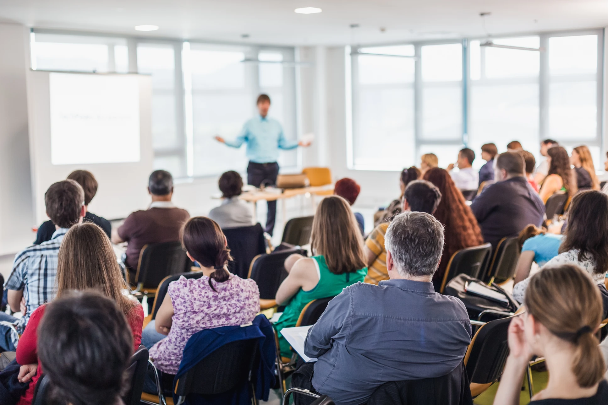 Salle de conférence moderne avec un formateur en chemise bleue présentant devant un public assis